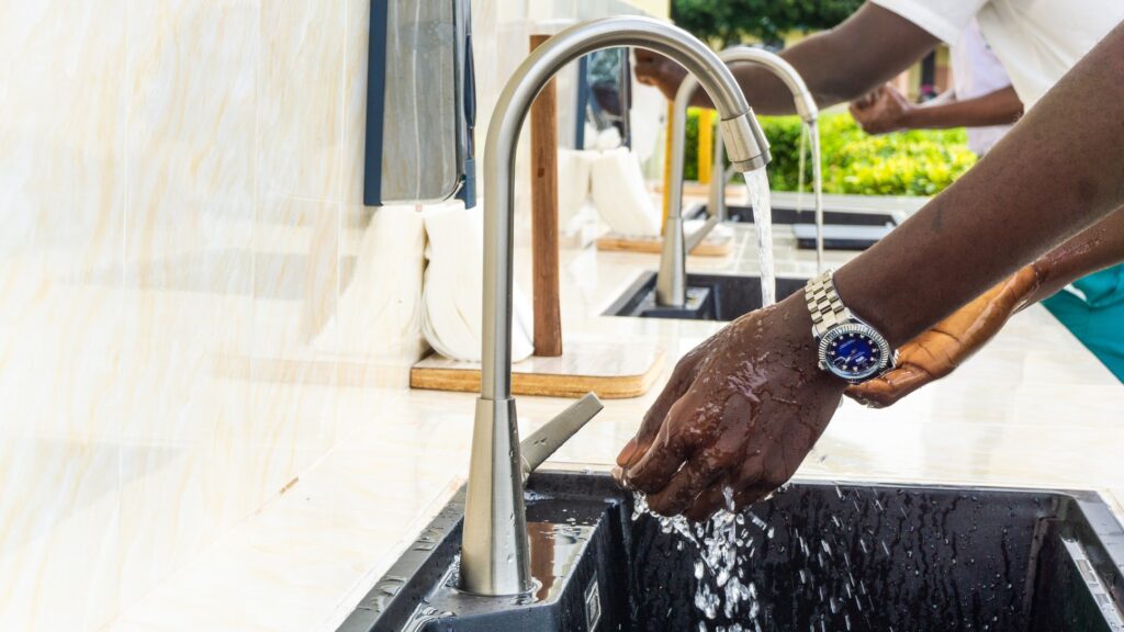 2 men with dark skin washing his hands under a faucet wearing a Rolex. A VPN is similar to the water flowing through the faucet.