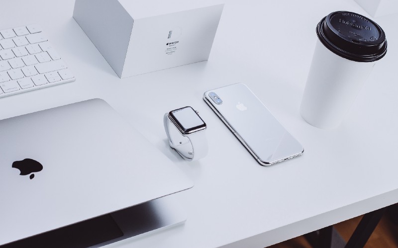 macbook apple watch iphone on white desk with coffee cup. These are all devices in apple's ecosystem