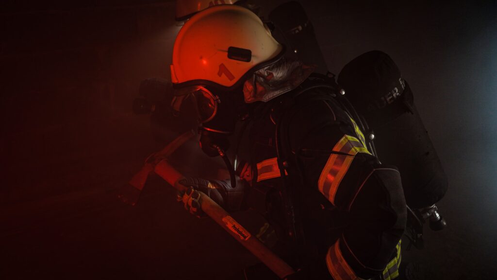 Firefighter with a yellow helmet and gas mask holding an axe walking into a fire. The fire represents a computer without a backup